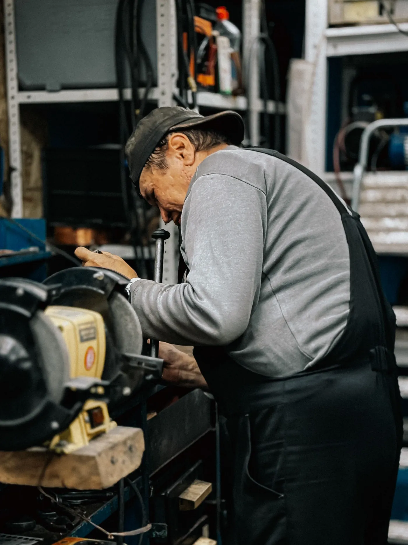 Ein älterer Mechaniker schleift ein Werkstück an der Schleifmaschine in seiner Werkstatt