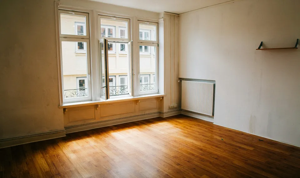 Leeres Altbauzimmer mit Holzdielen, dreiflügeligem Fenster zum Hof und Heizkörper